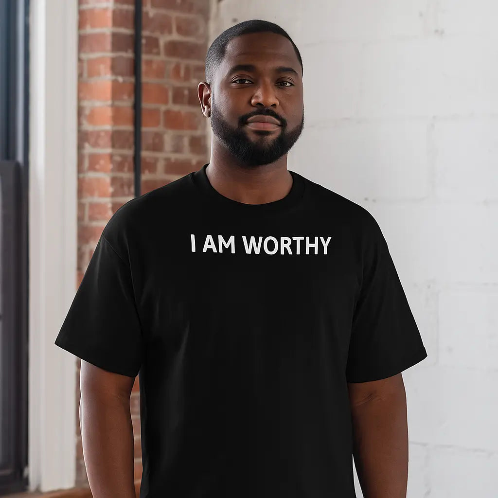 Man wearing a black t-shirt with 'I AM WORTHY' text against a brick wall.
